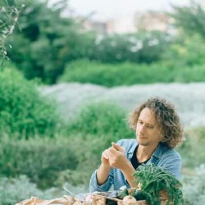 Man in Blue Long Sleeve Shirt Sitting By The Table With Basket Of Vegetables