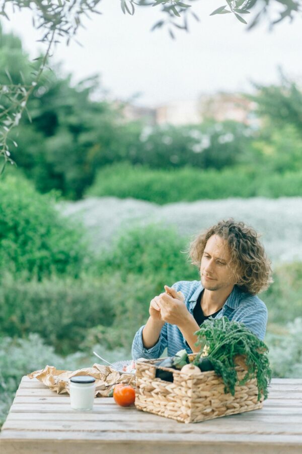 Man in Blue Long Sleeve Shirt Sitting By The Table With Basket Of Vegetables